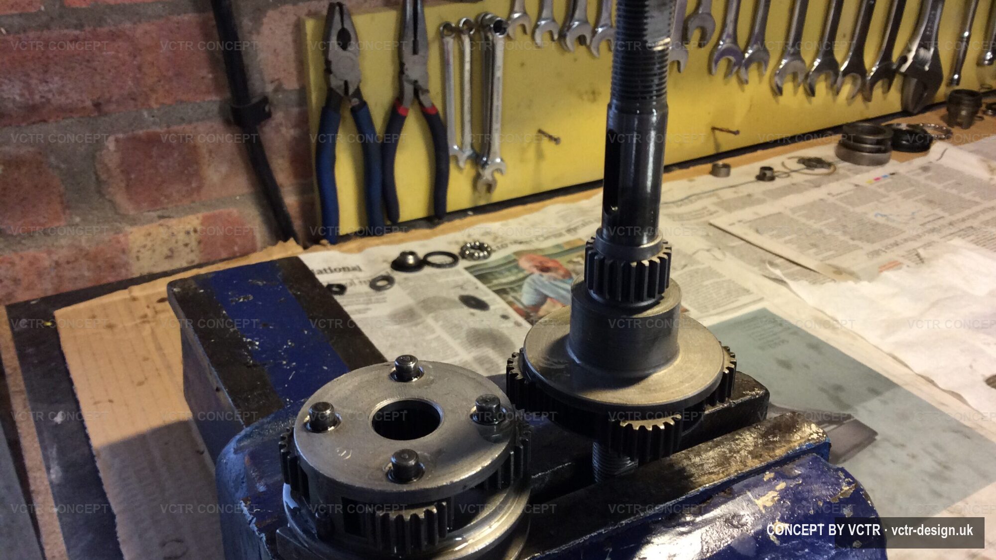 A hub gear held in the workshop vice in front of a wall of tools
